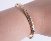 An 18ct yellow, white & rose gold twist design hinged bangle with push in clasp & figure of eight