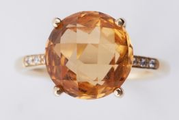 A yellow gold ring set with a central round fancy cut light orange semi-precious stone