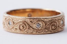 A 9ct yellow gold band with scroll designed engraving and small round cut diamonds