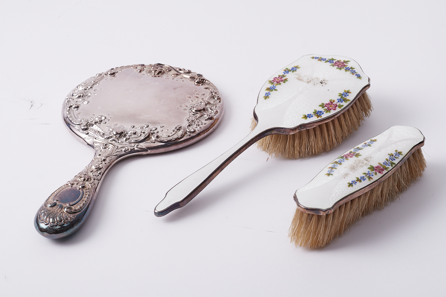A silver hand mirror together with two silver and enamel brushes (3).