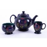A William Moorcroft teapot decorated with Pansy's together with milk jug and sugar bowl (3).