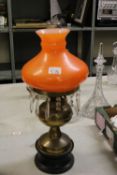 Late Victorian brass oil lamp: on wooden plinth base, with chimney and orange shade.