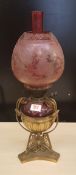 An Edwardian brass and cranberry glass oil lamp: standing on tri-form base, shade and chimney