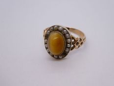 Unmarked yellow metal ring with oval tiger's eye surrounded seed pearls, AF, two pearls missing, siz