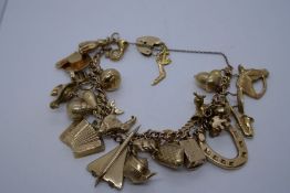 9ct yellow gold charm bracelet hung with 26 9ct gold charms to include (Concorde, Hohner accordion,