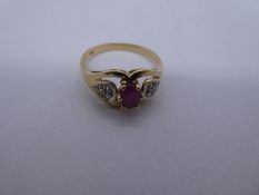 14ct yellow gold dress ring with central oval ruby flanked diamond chips, in heart shaped shoulders,