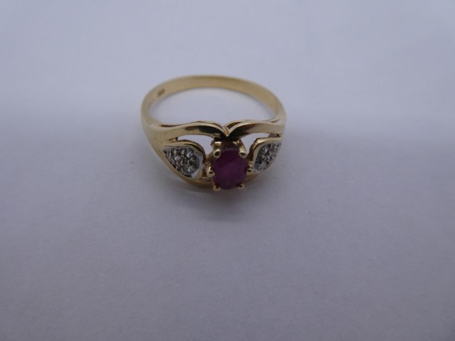 14ct yellow gold dress ring with central oval ruby flanked diamond chips, in heart shaped shoulders,