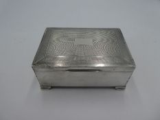 A heavy silver cigarette box with engine turned design lid and central vacant cartouch. On four pede