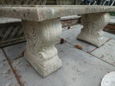 A reconstituted garden bench on pedestal supports