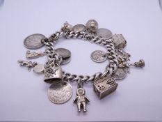 Silver charm bracelet hung with antique and later coins, charms etc including Fireman's helmet, ball