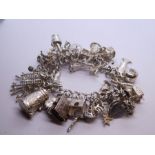 Silver charm bracelet hung with approx 34 charms to include cow bell, articulated fish, Bible, telep