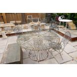 An ornate circular metalwork garden table with a set of six matching folding chairs