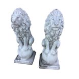 A pair of composition stone lions, the beasts sitting on their haunches with tails framing balls,
