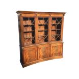 A reproduction mahogany concave fronted bookcase with moulded ogee dentil cornice supported on