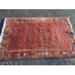 An oriental rug, the busy madder field woven with geometric bands, framed by flowerhead frieze on