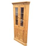 A pine corner cabinet with moulded cornice above a scalloped apron, having a pair of glazed doors