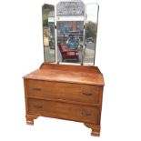 An oak dressing table with easel mirror to top flanked by hinged wings, the chest with two long