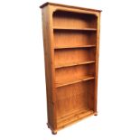 A pine open bookcase with moulded aprons framing five shelves, raised on plinth with bun feet. (37in
