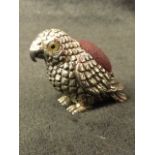 A sterling silver parrot pin cushion, the bird inset with glass eyes, having soft mound to back -