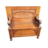 An oak monks bench with fielded panelled tabletop supported by carved lions revealing an oval floral