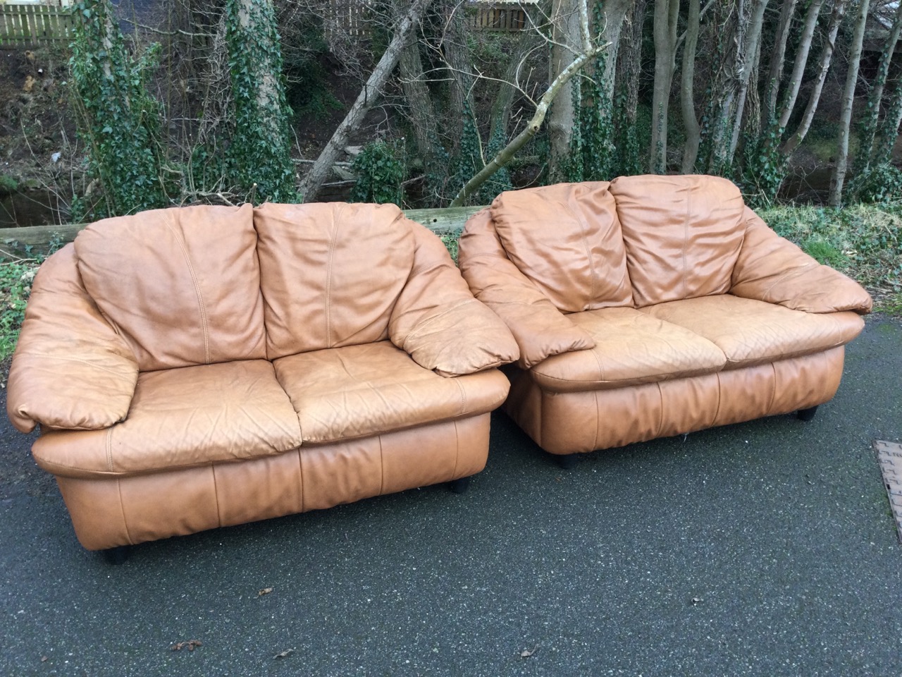 A pair of two-seater leather sofas with integral back, seat and armrest cushions, raised on