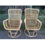 A pair of cane conservatory chairs with tapering spindle backs above curved seats and platform arms,