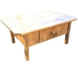 A pine coffee table with rectangular canted top above a deep apron with drawer, raised on square