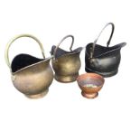 Three helmet shaped coal scuttles with swing handles - two in brass; and a circular copper bowl