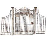 A heavy cast iron entranceway with wide gate and square pillars with side railings, the gate with