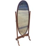 An oval mahogany cheval mirror supported on tapering columns with scrolled brass ring mounts, raised