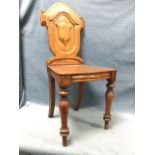 A Victorian oak hall chair with shield shaped back in scroll carved frame above a tapering seat,