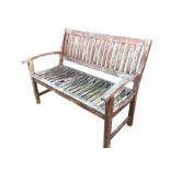 A slatted teak garden bench with arched arms raised on square column legs joined by rectangular