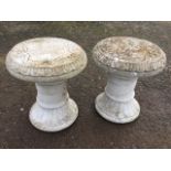 A pair of composition stone stools with circular lozenge moulded tops embossed with scrolling, on