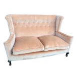 A Georgian style wing-back sofa with button studded upholstery and loose cushions, raised on