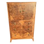 A 1950s walnut bedroom cabinet with crossbanded front, having caddy top above a cupboard and three