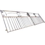 A pair of wide wrought iron driveway gates with scrolled panels above tubular spindles, all in