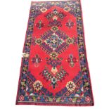 An oriental style rug woven with hooked medallions on red field within a leaf border on charcoal