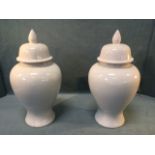 A pair of blanc-de-chine stoneware urns & covers, the baluster shaped pots with domed lids having