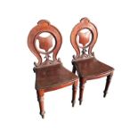 A pair of Victorian mahogany hall chairs with pierced oval backs, having shield shaped panels in