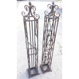 A pair of square decorative wrought iron garden towers with scrolled tops surmounted by berry