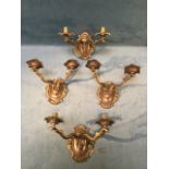 A set of four brass wall lights with oval scroll-cast wallplates supporting twin scrolled branches