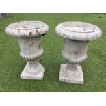 A pair of small composition stone garden urns, having overhanging lozenge rims on tapering fluted