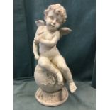 A winged cherub seated on leaf entwined ball support, raised on concave moulded plinth - resin. (