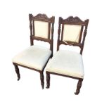 A pair of late Victorian oak chairs with scroll carved crests above upholstered panels in moulded