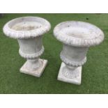 A pair of composition stone garden urns, the overhanging lozenge moulded rims on tapering fluted