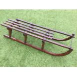 A C20th toboggan with slatted oak seat on angled tapering supports, the shaped runners with iron