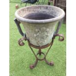 A ceramic urn on an associated wrought iron stand, the pot moulded with scrolled cartouches on