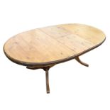 An oval Ducal pine dining table, the top extending with spare leaf, raised on twin turned columns