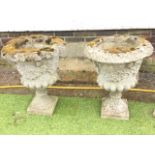 A pair of composition stone garden urns with overhanging rims, and floral garland moulded lobbed