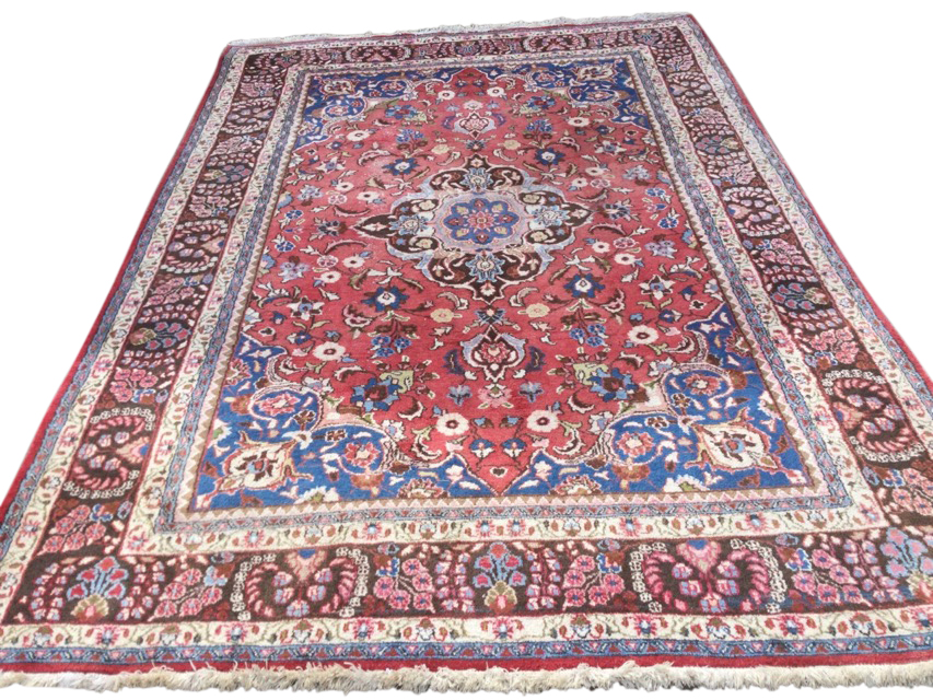 A large Indian rug woven with pink floral field having blue spandrels, framed by brown frieze of